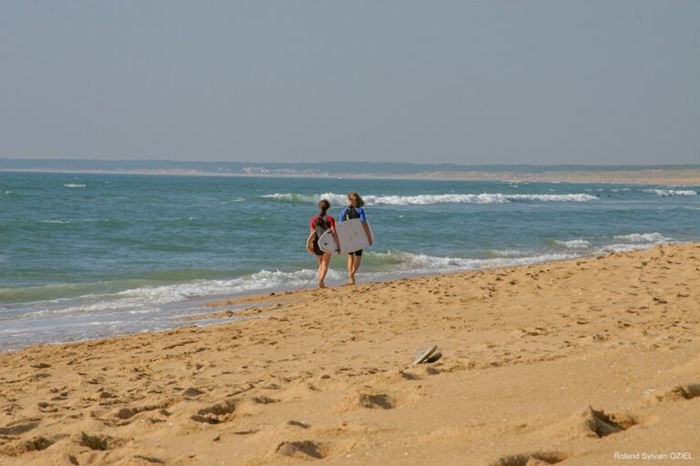 deux personnes qui longent la plage avec leur surf sous le bras
